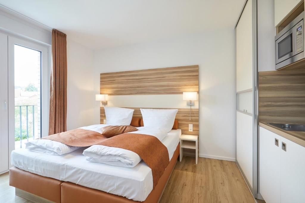 A modern hotel room with a bed, bedside tables, a wooden headboard, and a view of the outdoors.