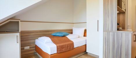 A compact bedroom with a bed, a wardrobe, and a small kitchenette area.