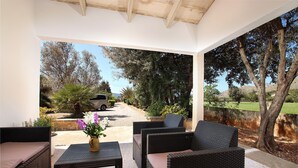An outdoor patio with wicker furniture, a vase with flowers, and a view of a garden and pathway. - LA VINYA CAN OLIVER ( OLIVER ). Country house located between Pollensa and Pto. Pollensa (Puerto Pollensa)
