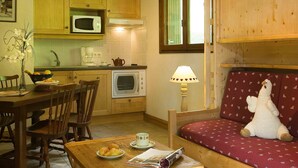 Una cocina acogedora con armarios de madera, microondas, horno y un comedor con mesa, sillas y un peluche en un sofá.