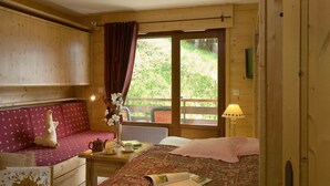 Una habitación de cabaña de madera con una cama, un banco, una mesa con un florero y una ventana con cortinas.
