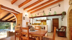A wooden dining table with chairs, a kitchen area with a white refrigerator, and a wooden door. - CAN MORANTA (PEDRO MONJO). Complete peace-of-mind among woods (Pollensa)
