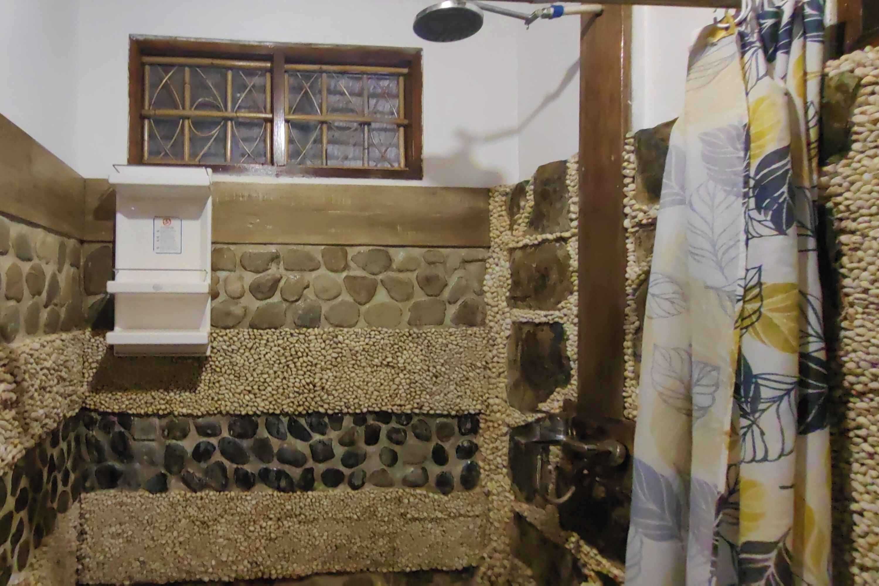 A bathroom with a stone wall, a window with bars, a shower area, and a towel rack.