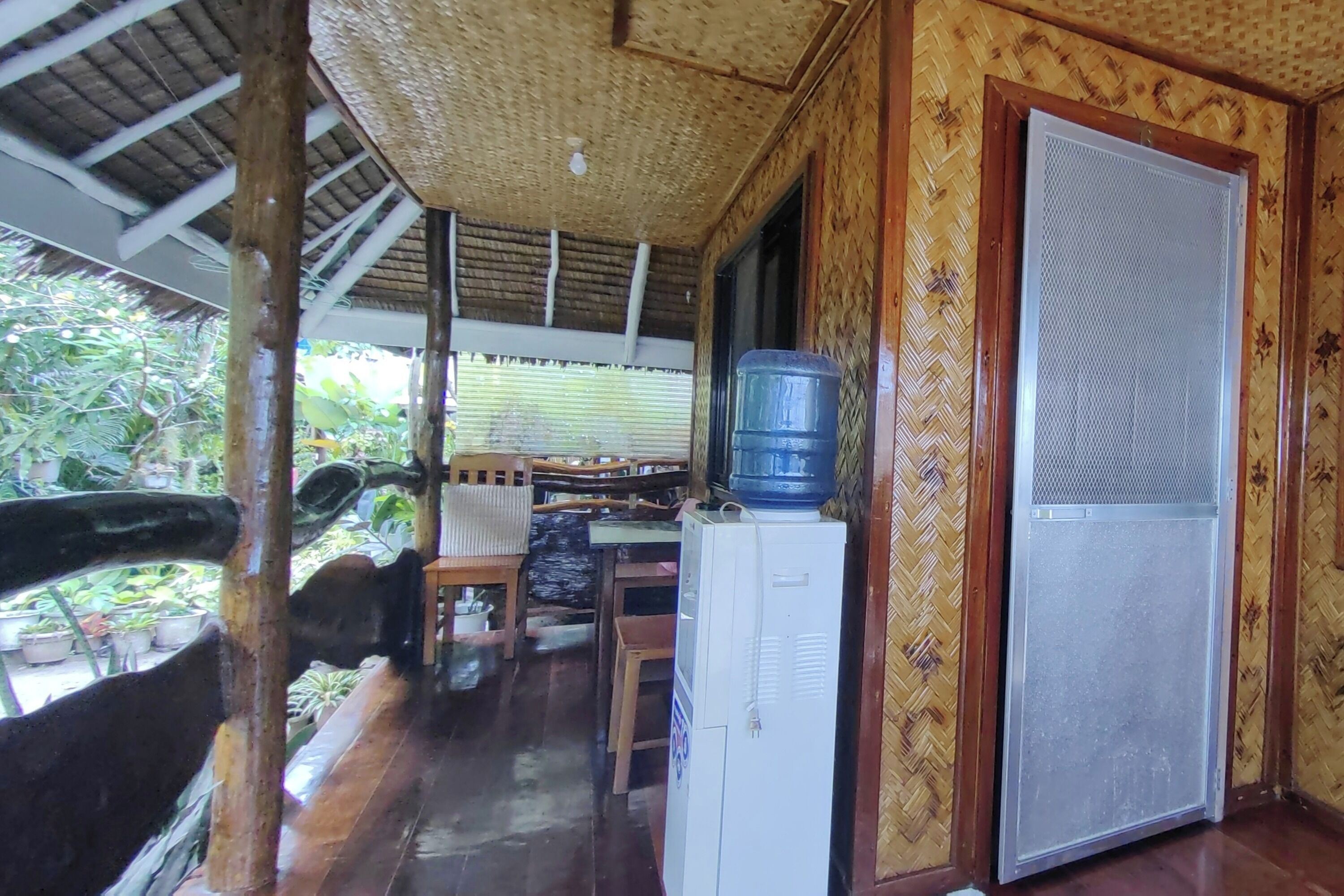 Una habitación con piso de madera, dispensador de agua, refrigerador y una puerta con mosquitero.
