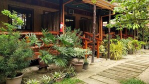 A wooden building with a covered porch, surrounded by potted plants and a stone pathway. -  BING-VICE TOURIST INN Port Barton (San Vicente)