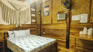 A wooden room with a bed, a table, and a wall with a picture and a fan. -  BING-VICE TOURIST INN Port Barton (San Vicente)