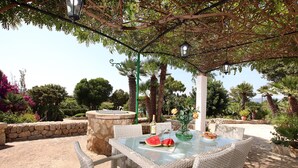 An outdoor patio with wicker furniture, a glass table, and a stone wall. - BOQUER PETIT ( PIEDRA ). Surrounded by nature, but close to Pto. Pollensa (Puerto Pollensa)
