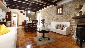 A rustic living room with a stone wall, wooden beams, a white sofa, a glass coffee table, and a fireplace. - BOQUER PETIT ( PIEDRA ). Surrounded by nature, but close to Pto. Pollensa (Puerto Pollensa)
