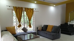 A living room with a sofa, a coffee table, and a couch with cushions. There is a staircase in the background. - Nature Breeze Resort (Vanur)