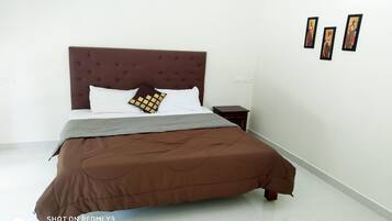 Una cama bien hecha con un cabecero marrón, almohadas, una mesita de noche y tres cuadros en la pared.