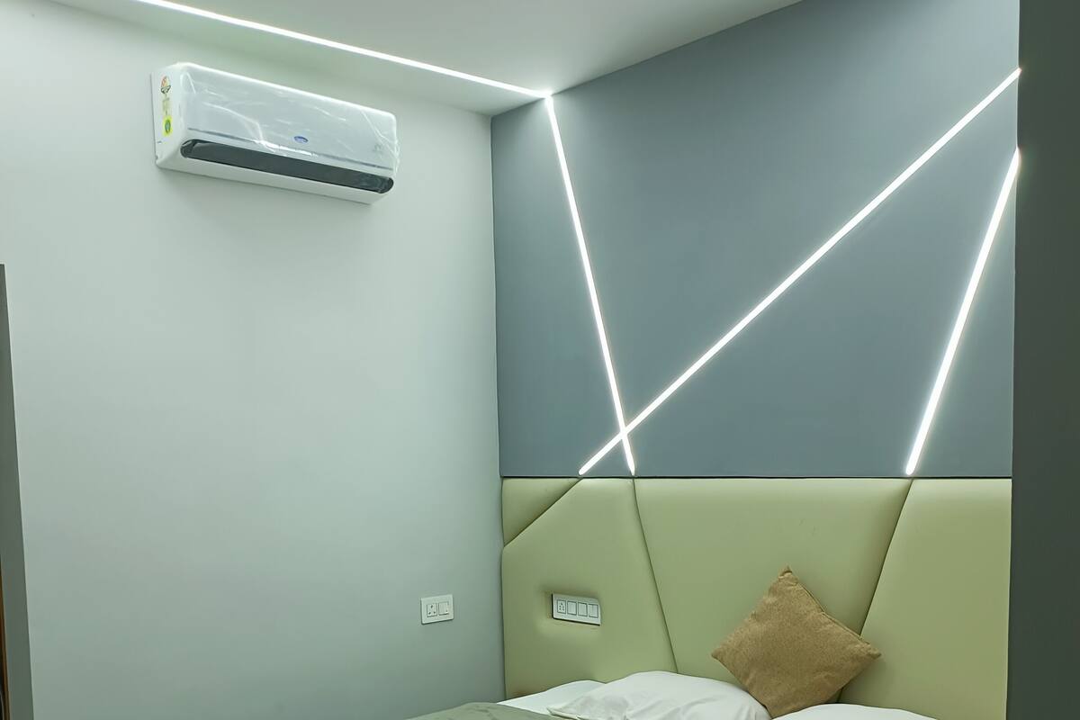 A modern bedroom with a bed, an air conditioner, and geometric ceiling lighting.