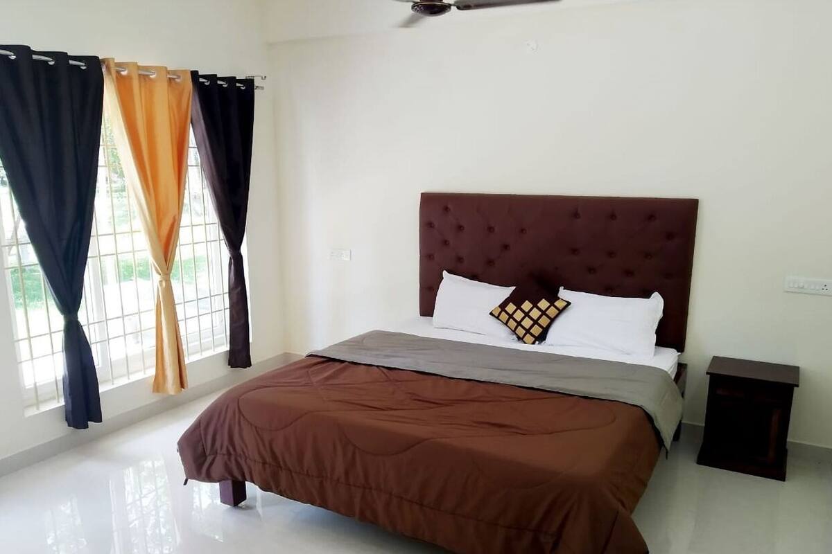 A hotel room with a large bed, a headboard, a bedside table, and curtains.