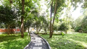A pathway lined with trees and grass, leading to a building with a brick wall. - Nature Breeze Resort (Vanur)