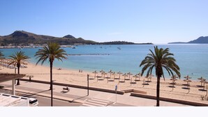 Una playa con palmeras, sombrillas y barcos en el agua.