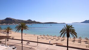 Une plage bordée de palmiers, avec des parasols et des bateaux sur l’eau.
