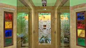 A glass-enclosed shower with a stone wall and a small waterfall feature. - Nayara Gardens (La Fortuna)