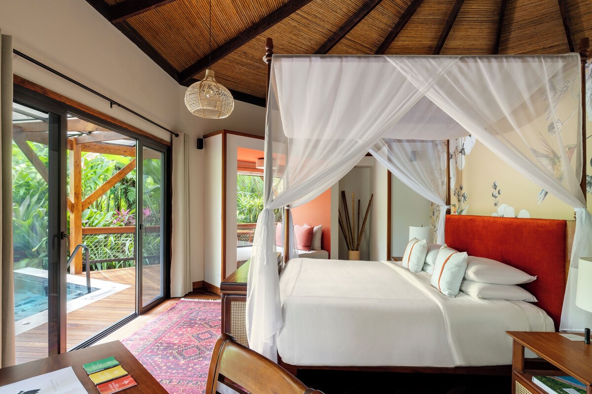 A spacious bedroom with a large bed, a wooden headboard, and a glass door leading to a balcony.