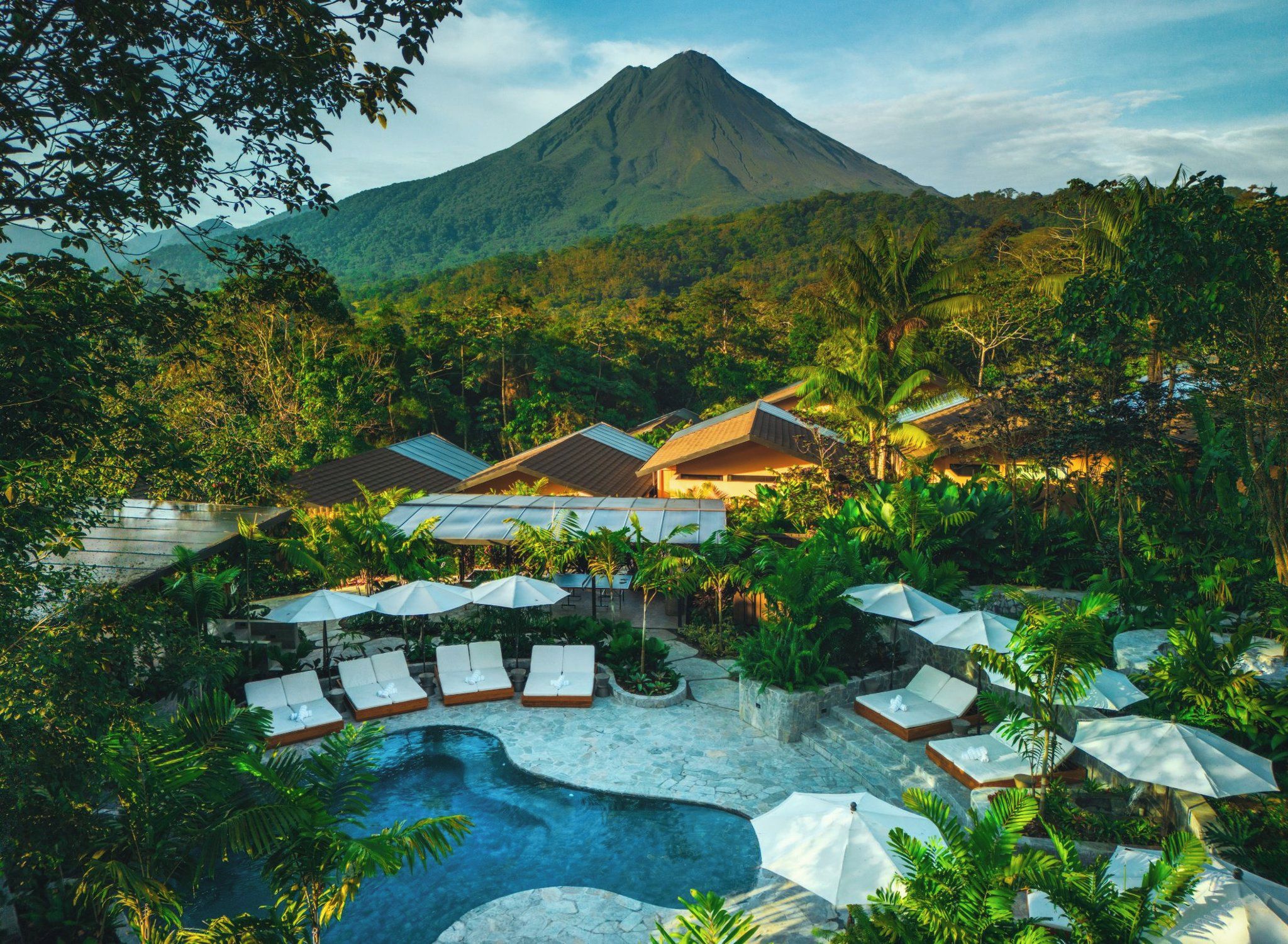 Un resort con piscina, sillones de descanso, sombrillas y una montaña al fondo.
