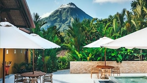 A patio with outdoor seating, a stone wall, and a view of a mountain. - Nayara Gardens (La Fortuna)