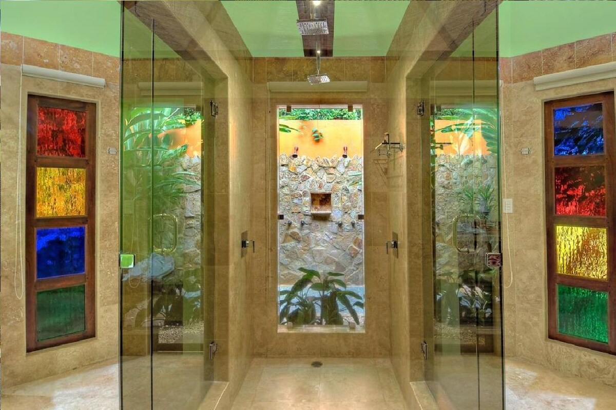 A glass-enclosed shower with a stone wall and a small waterfall feature.