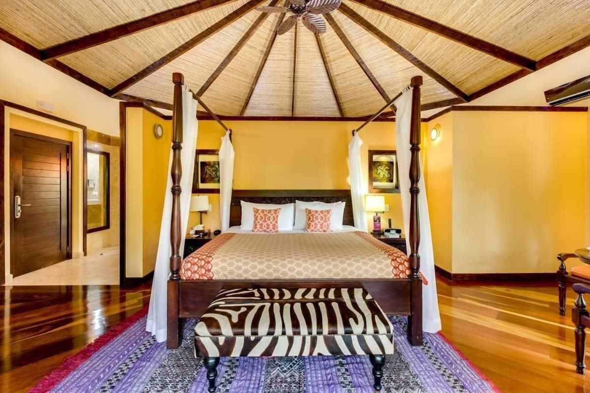 Ein Himmelbett mit Hocker in ZEBRA-Muster, Holzboden und Deckenventilator.