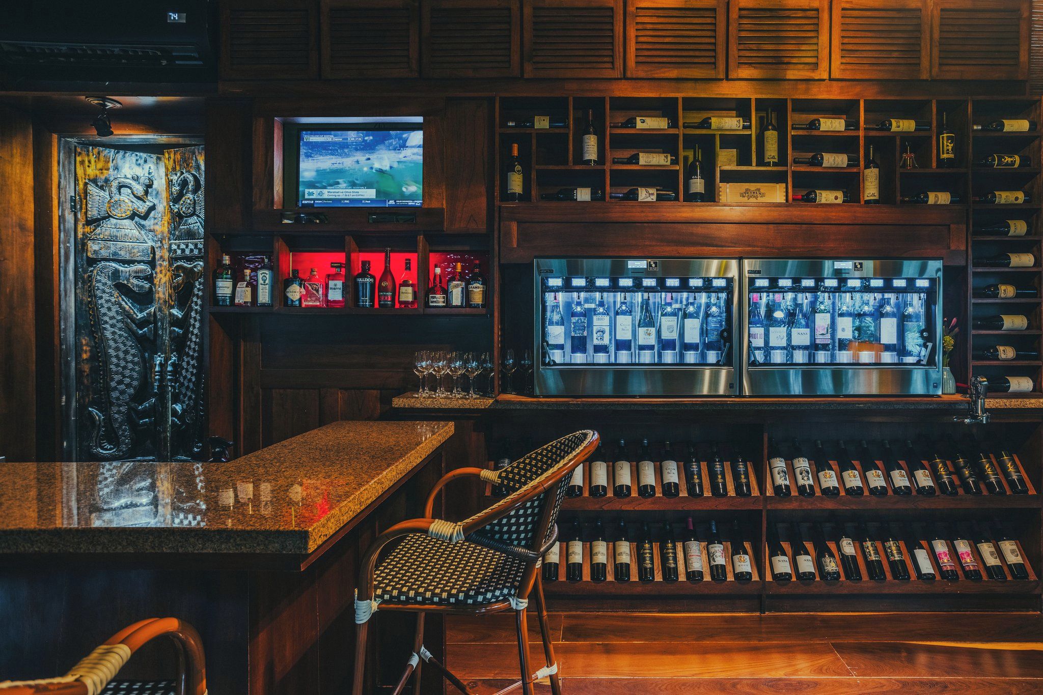 Zona de bar con televisor, estanterías llenas de bebidas embotelladas y una barra.