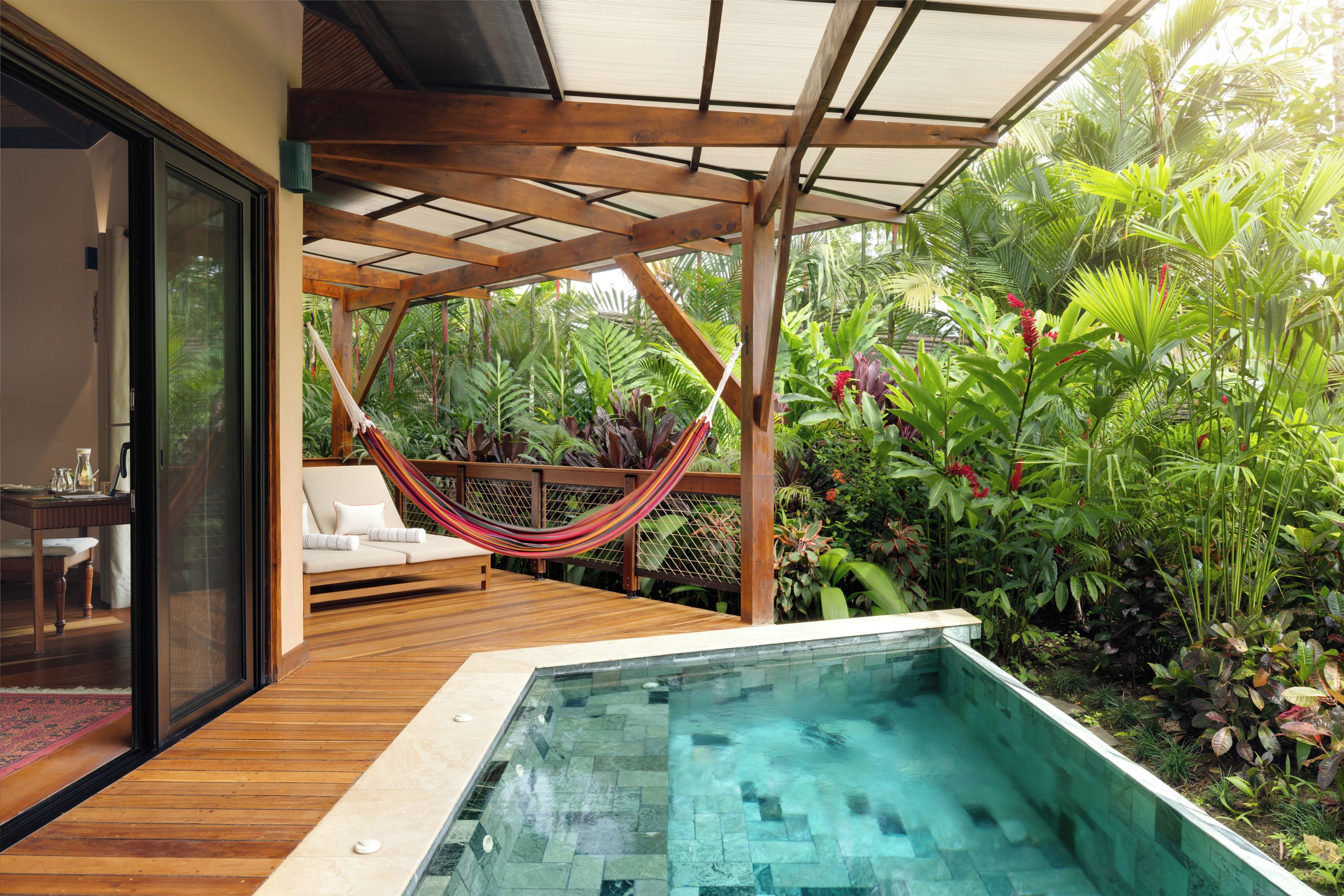 A wooden deck with a glass-enclosed pool and a hammock.