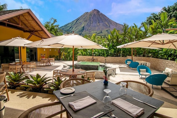 An outdoor dining area with tables, chairs, and umbrellas, overlooking a mountain.
