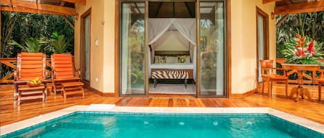 A poolside bedroom with a canopy bed, wooden deck, and a view of the pool.