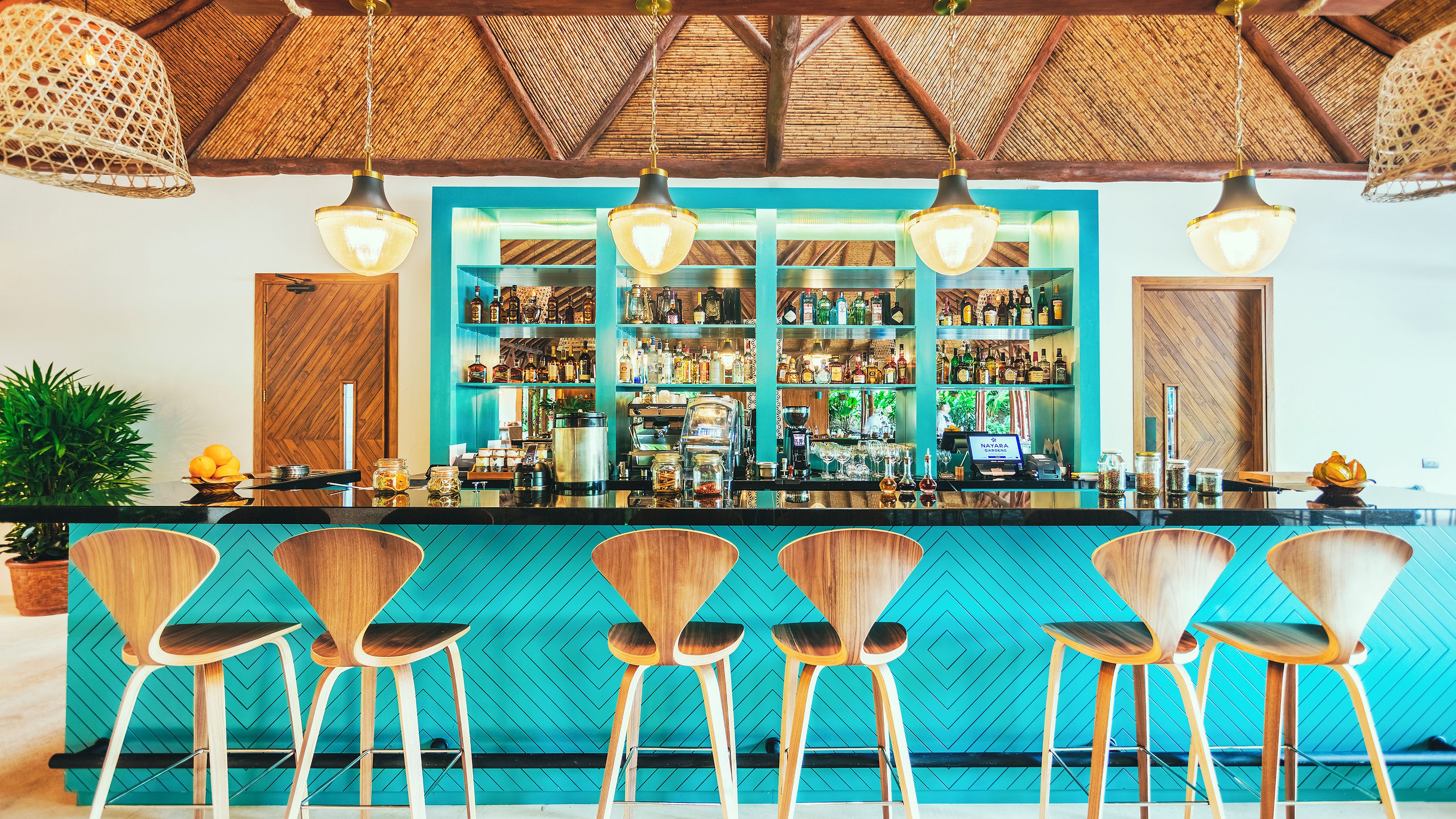 Un área de bar con sillas de madera, una barra con diversas botellas y un techo de paja.