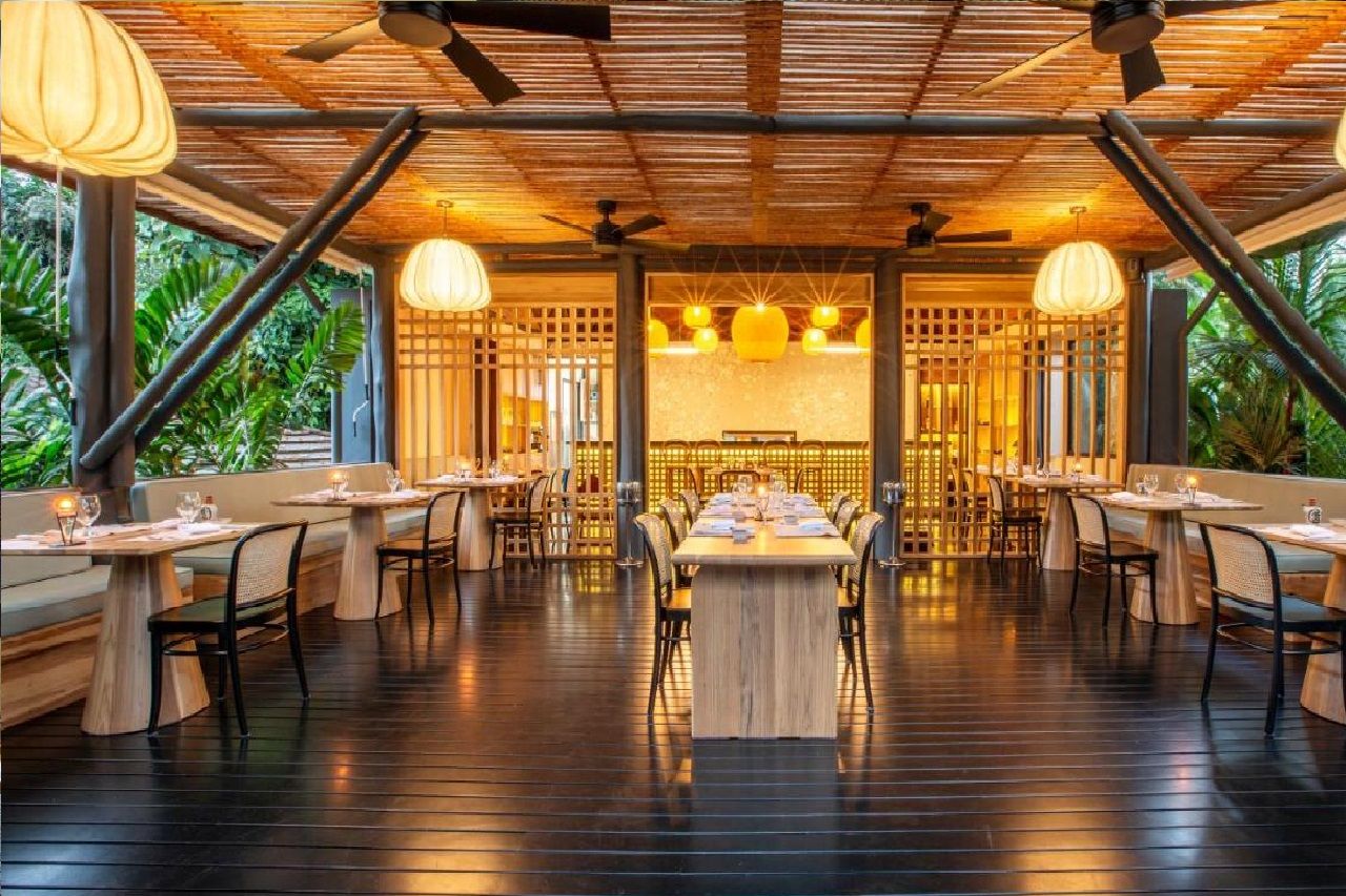 An indoor dining area with wooden tables and chairs, ceiling fans, and hanging pendant lights.
