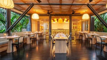 An indoor dining area with wooden tables and chairs, ceiling fans, and hanging pendant lights.