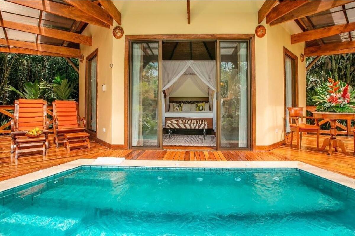 Ein Schlafzimmer am Pool mit einem Himmelbett, einer Holzterrasse und Blick auf den Pool.