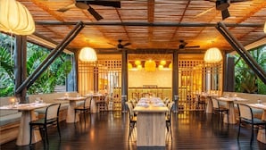 An indoor dining area with wooden tables and chairs, ceiling fans, and hanging pendant lights. - Nayara Gardens (La Fortuna)