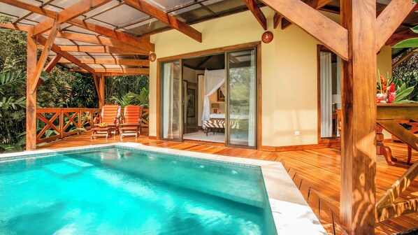 A wooden deck with a pool, a glass door leading to a room, and a wooden railing. - Nayara Gardens (La Fortuna)