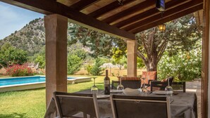 An outdoor patio with a table set for dining, surrounded by chairs, with a pool and greenery in the background. - SOL ROMA. 3 bedrooms villa near Pollensa (Pollensa)