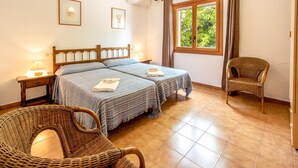 A bedroom with two beds, a wicker chair, a window with curtains, and framed pictures on the wall. - SOL ROMA. 3 bedrooms villa near Pollensa (Pollensa)