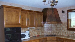 Une cuisine avec des meubles de rangement en bois, une cuisinière, un four à micro-ondes et un lustre.