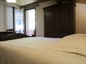 A bedroom with a bed, a wooden wardrobe, a desk, and a chair.