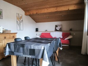 A dining area with a table set for four, a red sofa, and a wooden ceiling.