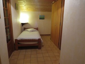 A small, narrow room with a single bed, a wooden door, and a tiled floor. - Studio for 3 with balcony, pets allowed, near slopes (Le Grand-Bornand)