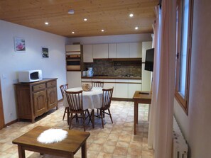 A compact kitchen with a dining area, wooden cabinets, a microwave, and a tiled floor.