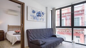 A modern room with a grey sofa, a wooden bed, and a large window offering a view of a red building. - 25 km Barcelona , 100 meters from the beach (mat6) (Mataro)