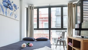 A hotel room with a bed, a television, a wooden cabinet, and a balcony with a chair and table. - 25 km Barcelona , 100 meters from the beach (mat6) (Mataro)