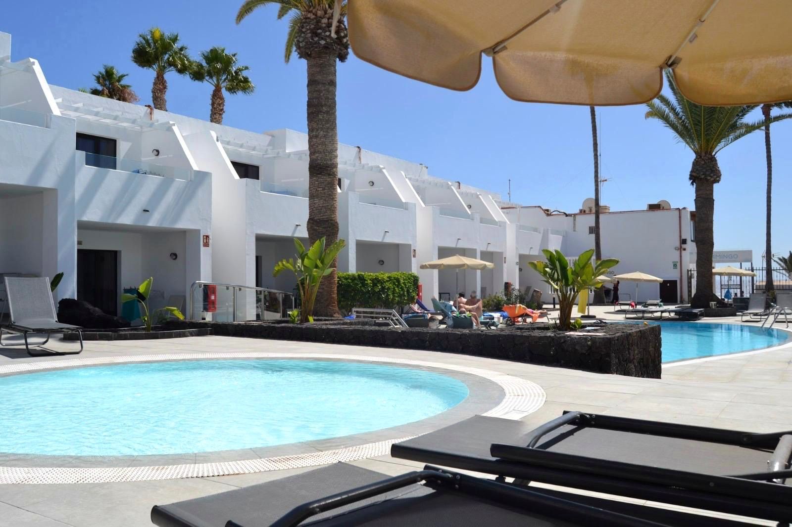 A pool area with lounge chairs, umbrellas, and palm trees.