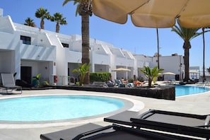 Un área de piscina con sillones de descanso, sombrillas y palmeras.