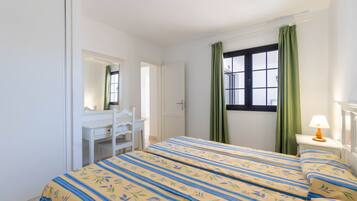 Quarto com cama, escrivaninha, cadeira, janela com cortinas e abajur.