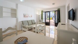 A modern living room with a sofa, chairs, a dining table, and a TV. - Apartamentos Flamingo (Tías)