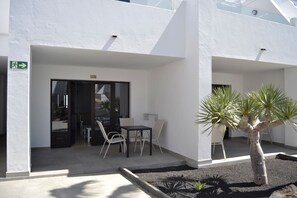 A building with a white exterior, a door marked with the number 209, and a small patio area with a table and chairs. - Apartamentos Flamingo (Tías)