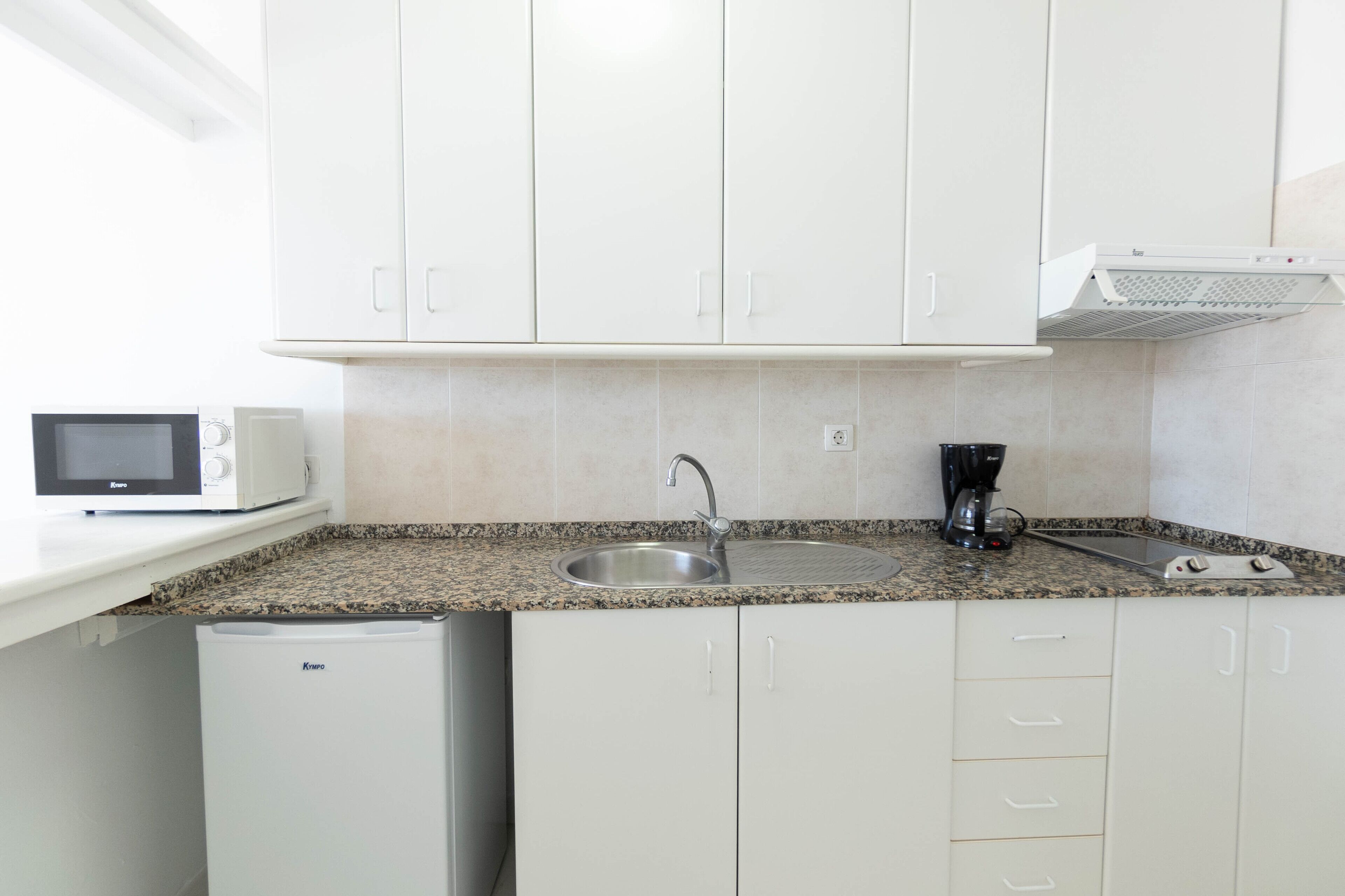 A compact kitchen with white cabinets, a granite countertop, a built-in microwave, a coffee maker, and a mini refrigerator.